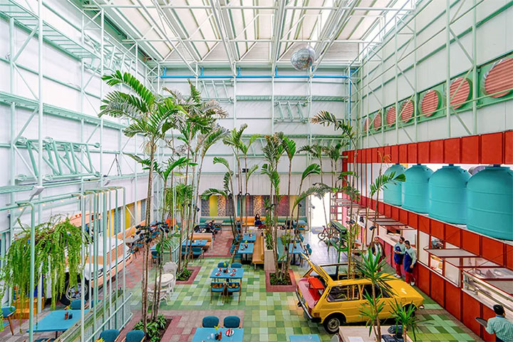Greenhouse-inspired cafe interior design with indoor plam trees, car and watertanks