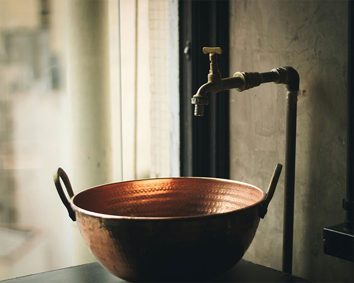 Copper sink against a concrete wall, as a great way to use copper as an accent metal in industrial interiors.