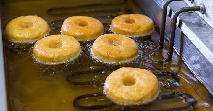 Donuts cooking in a tube-type commercial fryer.