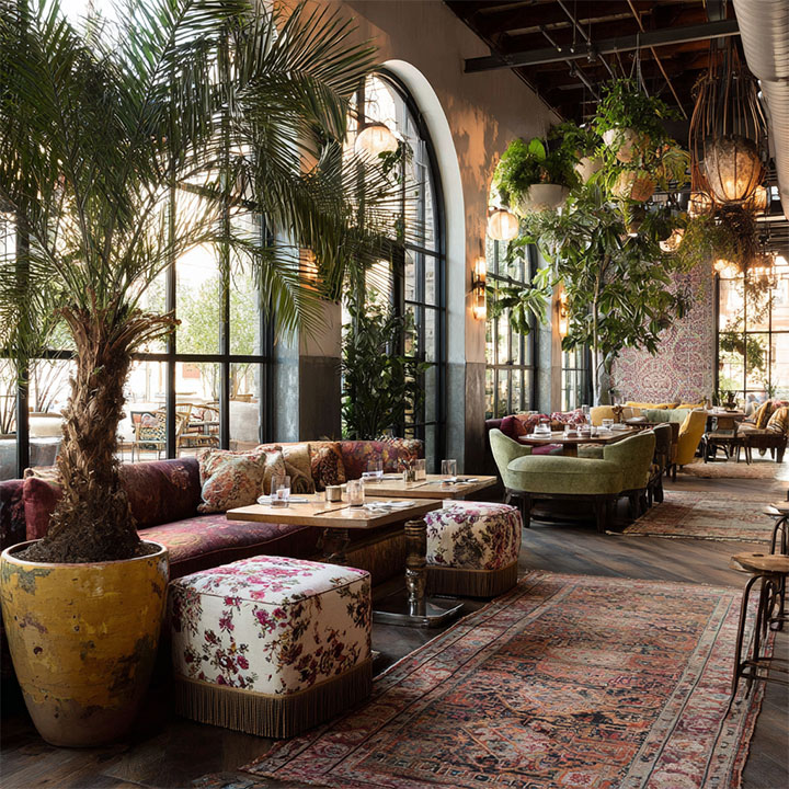 Potted trees and eclectic furniture in bohemian restaurant interior.